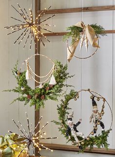 three christmas wreaths hanging from the side of a wooden wall with lights on them