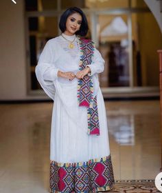 Ethiopian and Eritrean traditional dress,  elegant dress more vibrant and detailed embroidery. The patterns on the chest, cuffs, and hem are much more colorful, using a mix of red, yellow, green, black, and pink. The design on the neckline forms a prominent geometric motif, which is mirrored at the bottom of the dress and sleeves. The white fabric again serves as a canvas for these vivid details.  Any ceremony Traditional Embroidered Dress With Traditional Patterns, Traditional Embroidered Dress With Woven Motifs, Folk Style Traditional Wear For Eid Ceremonies, Eid Traditional Wear With Embroidered Border, Traditional Wedding Kaftan With Embroidered Border, Semi-stitched Dress With Embroidered Border For Traditional Ceremonies, Festive Kaftan For Traditional Ceremonies With Embroidered Border, Festive Embroidered Kaftan For Traditional Ceremonies, Traditional Kaftan With Embroidered Border