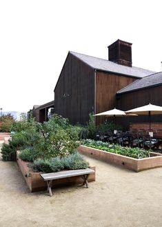 an outdoor dining area in front of a barn with tables and umbrellas on the patio