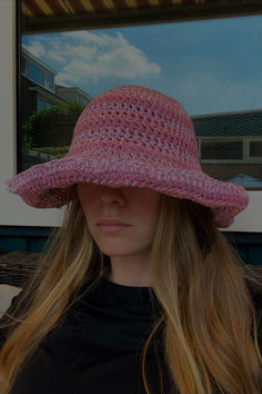 a woman with long hair wearing a pink hat in front of a window and looking at the camera