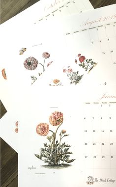 three calendars with flowers on them sitting on top of a wooden table next to each other