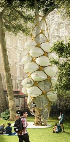 a man standing next to a tree with plates hanging from it's sides and people sitting on the grass