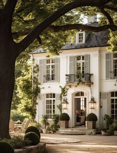 a large white house with lots of windows and plants on the front door, surrounded by trees