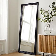 a large black framed mirror sitting on top of a wooden table next to a plant