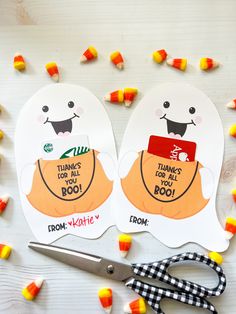 two paper cutouts with candy corn on the table next to scissors and some candy