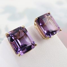 "Natural sparkling purple amethyst gems are basket-set in this vintage pair of 14k yellow gold stud earrings. Each 6 carat faceted rectangular amethyst measures approx. 12mm x 10mm x 7.5mm. The stones are of lovely semi-translucent medium purple color with a slight reddish hue. Together they have a 12 carat total weight in amethyst. The airy sturdy setting shows of the genuine stones nicely. The earring settings and push-on backs are all marked, \"14k\" (gold) and there is an unknown maker's mark on the back of the settings. Overall, this pair is in very good vintage condition with minor pre-owned wear and a slight irregularity to straightness of one post. Please see all photos and below for detailed measurements. This pair would bring a nice pop of color to your ears! Total Wt: 4.4 grams Purple Rectangular Jewelry For Formal Occasions, Formal Rectangular Purple Jewelry, Formal Purple Rectangular Jewelry, Classic Square Cut Purple Jewelry, Classic Purple Jewelry With Rectangular Stone, Purple Rectangular Jewelry With Prong Setting, Classic Purple Square Cut Jewelry, Yellow Gold Stud Earrings, Amethyst Studs