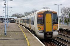 a yellow and white train traveling down tracks next to a loading platform at a train station