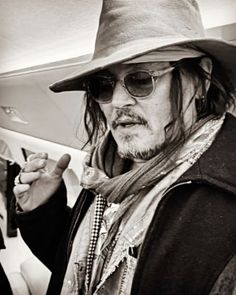 a man with long hair wearing a hat and sunglasses pointing at something in his hand