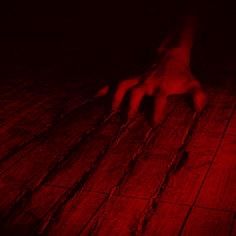 a person's hand on the floor with red light coming from behind it in a dark room