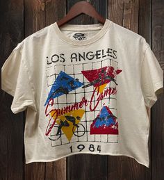 Los Angeles Summer games 1984 relaxed Cropped T- shirt available in Natural color This Crop Jersey Tee slides right into streetwear style for Summer and Winter.. With oversized sleeves and a relaxed body, this on-trend tee drops a little lower in the back for an effortlessly cool feel. Fabricated from ultra-soft, lightweight Airlume cotton that's fit to flatter, this looser crop features a finished hem and neck binding.Features: Cut off bottom. Oversized sleeves. Neck binding. Relaxed body.Fabrication: 100% Airlume combed and ring-spun cotton Sizing- Small -15 inches neck to bottom- 21 inches wide Medium- 16 inces neck to bottom- 22 inches wide Large- 17 inches neck to bottom- 23 inches wide X-Large- 18 inches neck to bottom-24 inches wide Los Angeles Summer, Oversized Sleeves, Surf Tee, Oversize Sleeves, Summer Games, Crop T Shirt, Streetwear Style, Jersey Tee, Crop Tshirt