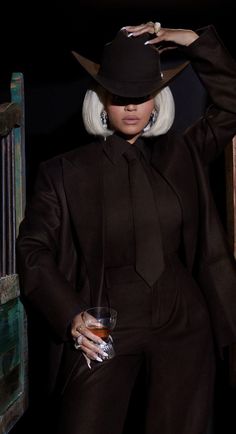 a woman in a black suit and hat holding a drink