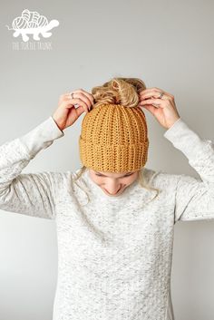 a woman wearing a knitted beanie and holding her hair in front of her head