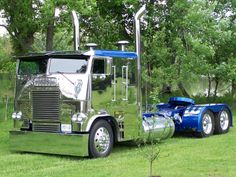 a large green semi truck parked on top of a lush green field next to trees