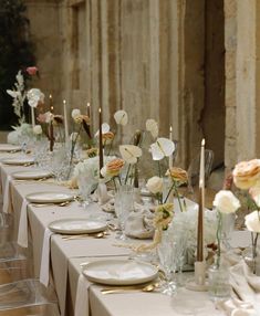 a long table is set with white and gold plates, silverware, and flowers