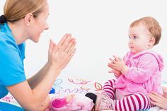 a woman in blue shirt sitting next to a baby on the floor with her hands together