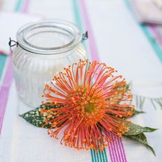 an orange flower sitting on top of a table next to a glass jar filled with liquid