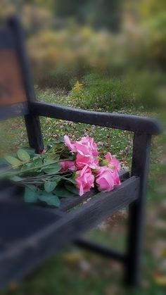 some pink flowers are sitting on a black bench in front of green grass and trees