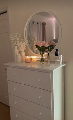 a white dresser with flowers and candles on it