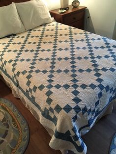 a bed with a blue and white quilt on top of it next to a night stand