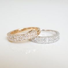 two gold and white diamond wedding rings sitting on top of each other in front of a white background