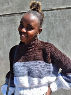 a smiling woman wearing a sweater and carrying a purse in her hand while standing next to a concrete wall