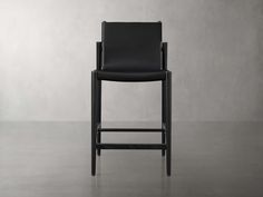 a black leather bar stool in front of a gray wall with no one sitting on it