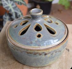 a ceramic container sitting on top of a wooden table next to a potted plant