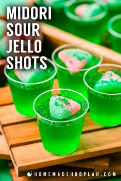 green jello shots with heart shaped candies in them on a wooden tray and text overlay reads midori sour jello shots