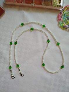 a white beaded necklace with green beads and scissors next to it on a table