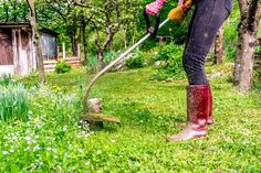 a woman in rubber boots is cutting grass with a lawnmower