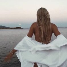 a woman in white dress sitting on the edge of a boat looking out to sea