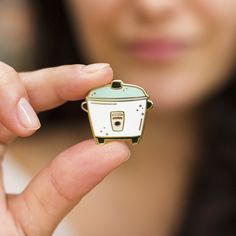 a woman is holding a small white and blue crock pot brooch in her hand