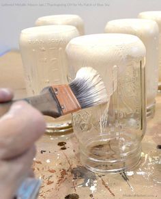 someone is painting glass jars with paintbrushes