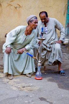 two men are sitting on the ground and one is holding an oil burner while the other man looks at it