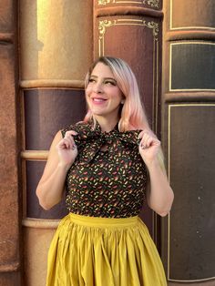 a close up of a model standing in front of books wearing leaves bow top and holding the ties of the bow Cotton Tie Neck Tops For Fall, Fall Cotton Top With Bow Detail, Retro Sleeveless Tops For Fall, Retro Sleeveless Fall Tops, Spring Retro Tie Neck Tops, Spring Retro Tie-neck Tops, Retro Tie Neck Tops For Spring, Shirred Skirt, Retro Pin Up