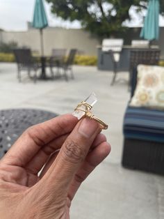 a person holding a ring in their hand near an outdoor table and chairs with umbrellas