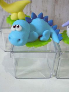 three plastic dinosaurs sitting on top of each other in clear containers with green plants and blue ones