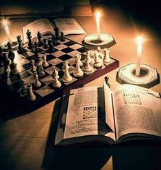 an open book sitting on top of a wooden table next to chess pieces and candles