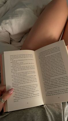 a woman laying in bed with her legs crossed and holding an open book next to her