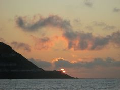 the sun is setting over an island in the middle of the ocean with some clouds