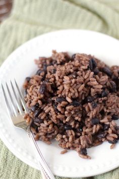 a white plate topped with rice and raisins next to a knife and fork