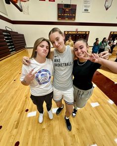 three girls standing on a basketball court posing for the camera with their hands in the air