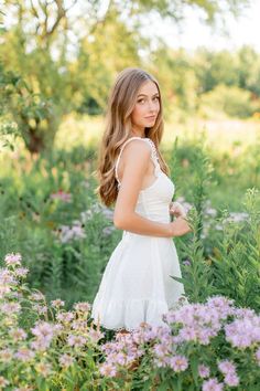 a beautiful young woman in a white dress standing among wildflowers at the park