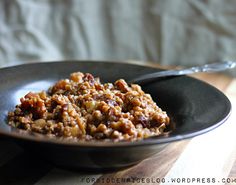 a black bowl filled with food sitting on top of a wooden table next to a spoon