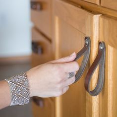 a woman's hand is opening the drawer with a pair of brown leather handles