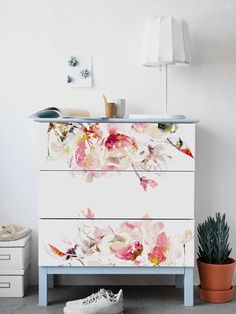 a white dresser with pink flowers painted on the front and bottom, next to a potted plant