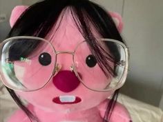 a pink teddy bear wearing glasses on top of a bed