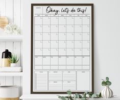 a calendar hanging on the wall next to a potted plant and bookshelf