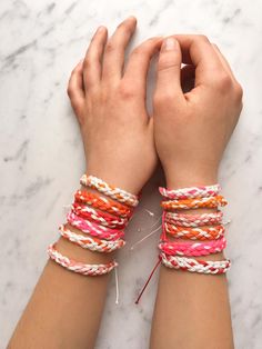 two hands with bracelets on top of a marble table next to scissors and thread