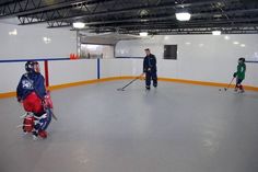 an ice hockey rink with two men and one boy playing on the ice while another man watches